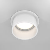 The Reif Round Recessed Downlight with Extended Rim - White is elegantly illuminated and seamlessly fits into a smooth, light-colored ceiling.