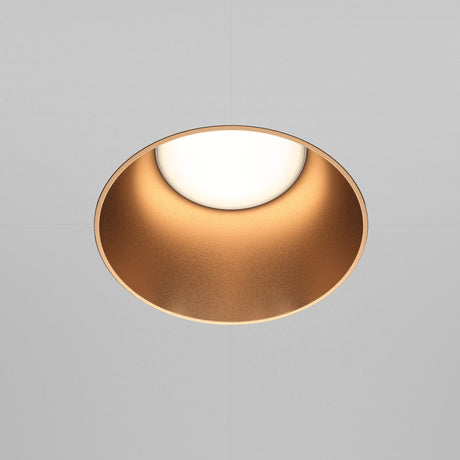 The Share Round Plaster-in Fixed Recessed Downlight in matte gold adds a soft, warm glow against a neutral gray ceiling with its circular design and seamless plaster-in installation.