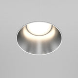 The Share Round Plaster-in Fixed Recessed Downlight, boasting a minimalist design, features a matte silver finish and a glowing white center against a plain white ceiling.