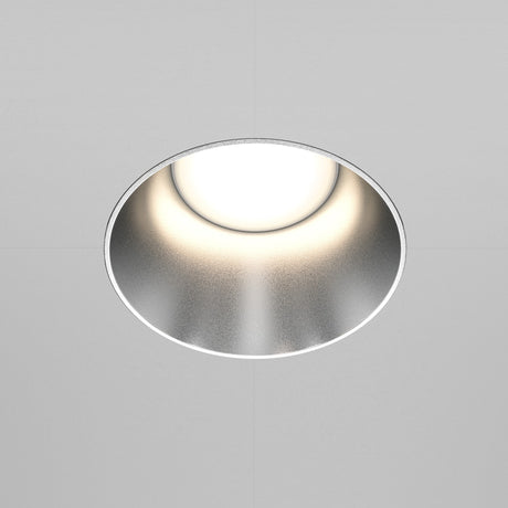 The Share Round Plaster-in Fixed Recessed Downlight, boasting a minimalist design, features a matte silver finish and a glowing white center against a plain white ceiling.