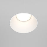 The Share Round Plaster-in Fixed Recessed Downlight - White, with its minimalist round design, casts a soft glow, enhancing the understated elegance of the surrounding white ceiling.