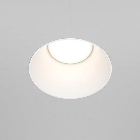 The Share Round Plaster-in Fixed Recessed Downlight - White, with its minimalist round design, casts a soft glow, enhancing the understated elegance of the surrounding white ceiling.