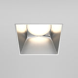 The Share Square Plaster-in Fixed Recessed Downlight in matte silver features a centered round bulb, emitting a soft white glow that enhances modern interiors and complements smooth, gray-toned ceilings.
