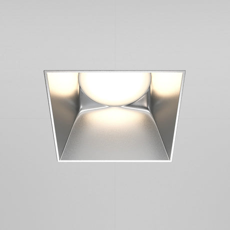 The Share Square Plaster-in Fixed Recessed Downlight in matte silver features a centered round bulb, emitting a soft white glow that enhances modern interiors and complements smooth, gray-toned ceilings.