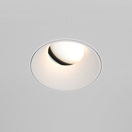 The Share Round Plaster-in Recessed Swivel Downlight in white has a circular trim with a slightly angled bulb for a soft glow. Embedded in a smooth white ceiling, it offers adjustable light direction for versatile illumination.
