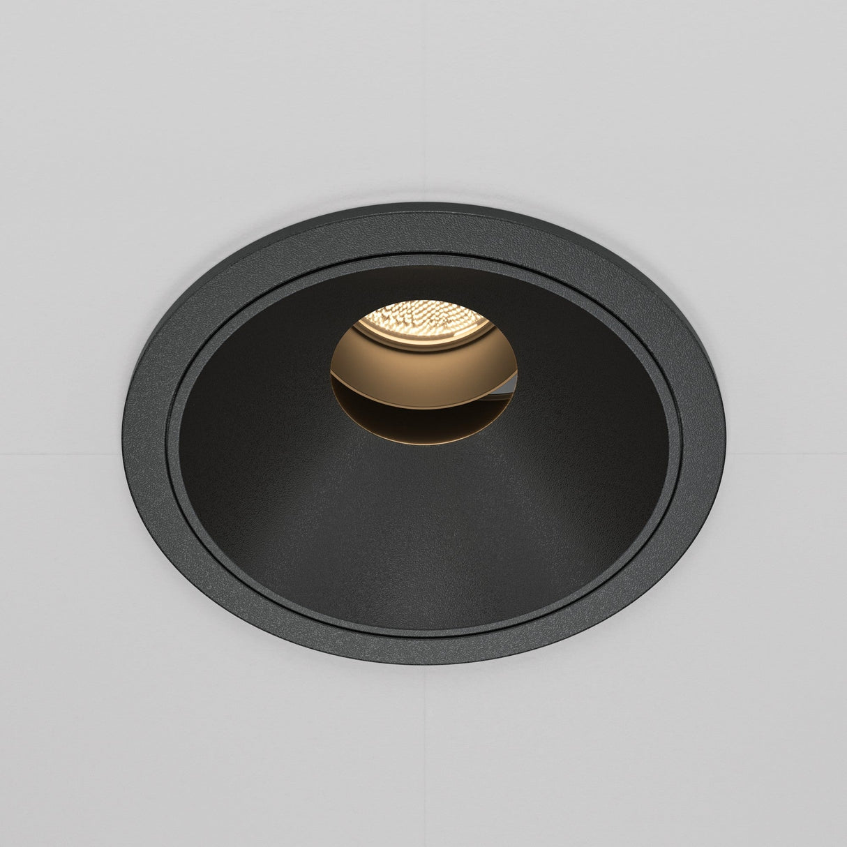 The Wise LED Round Recessed Downlight 10W 3000K - Black showcases a minimalist design with its black circular frame on a white surface, emitting a warm glow that creates an inviting atmosphere, enhanced by its high Colour Rendering Index (CRI).