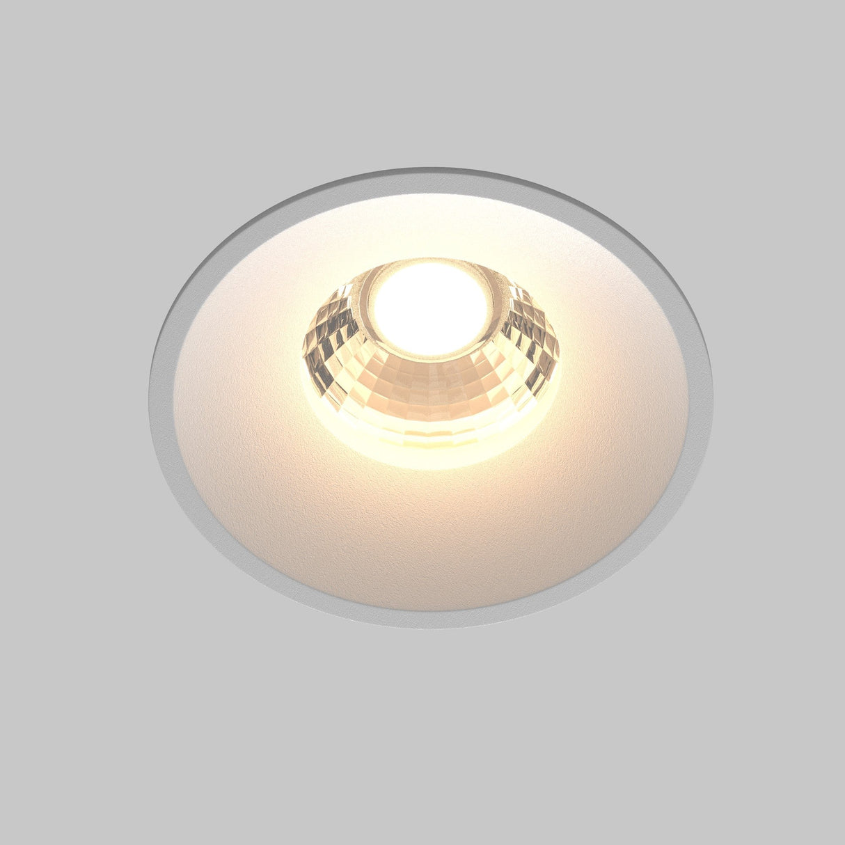 The Round LED Recessed Downlight 12W 3000K - White features a faceted reflector, casting a warm glow against a light gray backdrop, ideal for contemporary lighting in minimalist interiors.