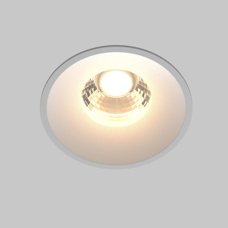 The Round LED Recessed Downlight 12W 3000K - White features a faceted reflector, casting a warm glow against a light gray backdrop, ideal for contemporary lighting in minimalist interiors.