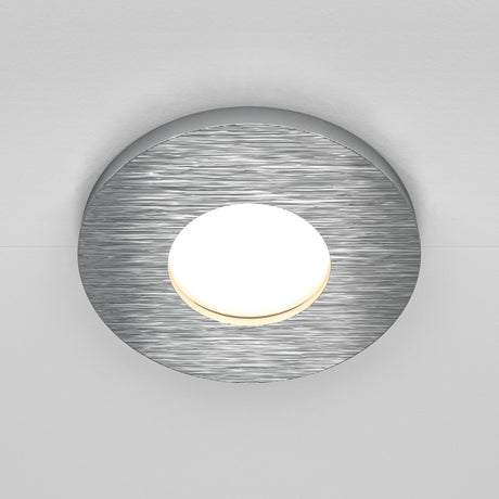 The Stark Fixed Round Recessed Downlight in silver features a modern brushed metal frame with a glowing center, perfectly mounted on a white ceiling. Its compatible with GU10 bulbs for versatile lighting options.