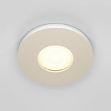 The Stark Fixed Round Recessed Downlight - White, featuring a glowing GU10 bulb, is set in a smooth surface. Its modern design emits soft, warm light and boasts an IP65 rating for dependable use in moist areas.