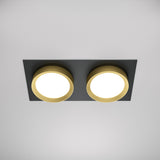 The Hoop Twin Fixed Rectangular Recessed Downlight in black and gold elegantly accents a white ceiling with its dual round lights on a sleek base, embodying the timeless allure of these two classic colors.