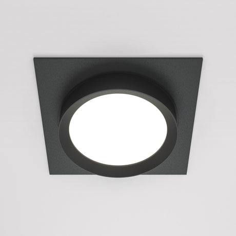 The Hoop Single Fixed Square Recessed Downlight in black features a round, illuminated center that provides energy-efficient LED lighting. Its modern, minimalist design looks elegant against a white ceiling.