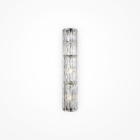 The Facet 3 Light Long Wall Light in chrome is a vertical cylindrical glass sconce with crystal and faceted panel detailing, emitting a soft, diffused light. Mounted on a plain white wall, it adds an elegant and modern touch to any space.