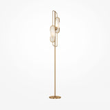 The Marmo 2 Light Floor Lamp - Brass features a slim brass frame with two abstract elongated light fixtures. It includes a natural stone accent, standing on a round base against a white backdrop—ideal for modern interiors.