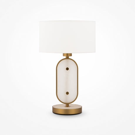 The Marmo Table Lamp in gold features a white cylindrical lampshade, a stylish base with a gold frame surrounding an oval natural stone panel, and rests on a circular gold platform.