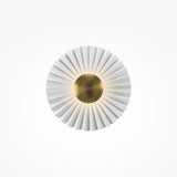 The Fiore Dimmable LED Circle Disc Wall Light in Brass is illustrated against a plain white background, featuring a circular pleated white lampshade with a metallic gold center, resembling a stylized flower or sunburst.