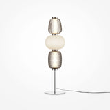 The Pattern LED Table Lamp - Chrome offers a modern look with its chrome finish and metallic base, featuring three stacked glass shades: textured clear on top, smooth white in the middle, and textured amber at the bottom. A black power cord enhances its contemporary appeal.