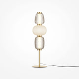 The Pattern LED Table Lamp - Gold features a sleek brass base with gold metal fittings, three stacked glass elements (two clear with textured patterns and one opaque white in the center), and an energy-efficient black cord extending from the base.