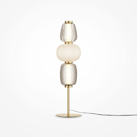 The Pattern LED Table Lamp - Gold features a sleek brass base with gold metal fittings, three stacked glass elements (two clear with textured patterns and one opaque white in the center), and an energy-efficient black cord extending from the base.