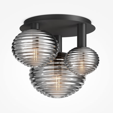 The Reels 3 Light Semi-Flush - Black is a modern ceiling fixture with three differently sized ribbed glass globes, exuding an industrial design. Its metallic sheen and visible bulbs create a warm glow from its circular base, embodying semi-flush lighting.