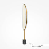 The Breeze LED Floor Lamp - Brass features a slim, oval-shaped LED light fixture for energy-efficient lighting. Its mounted on a sleek brass stand with a cylindrical black marble base, and it includes a black power cord and switch nearby.