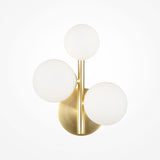 The Dallas 3 Light Wall Light features a brass base and three white opal glass globes arranged in a triangular pattern, combining metallic and matte finishes for contemporary flair.