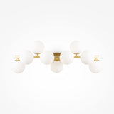 The Dallas 9 Light Wall Light features a sleek brass frame with nine evenly spaced white opal glass globes, creating a symmetrical design ideal for ambient lighting against a white backdrop.