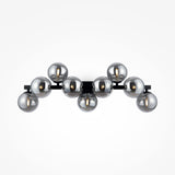 The Dallas 9 Light Wall Light features a black frame with nine metallic spheres and smoked mirrored glass, elegantly arranged in a symmetrical design, making it the perfect complement to any modern interior lighting scheme against a plain white background.