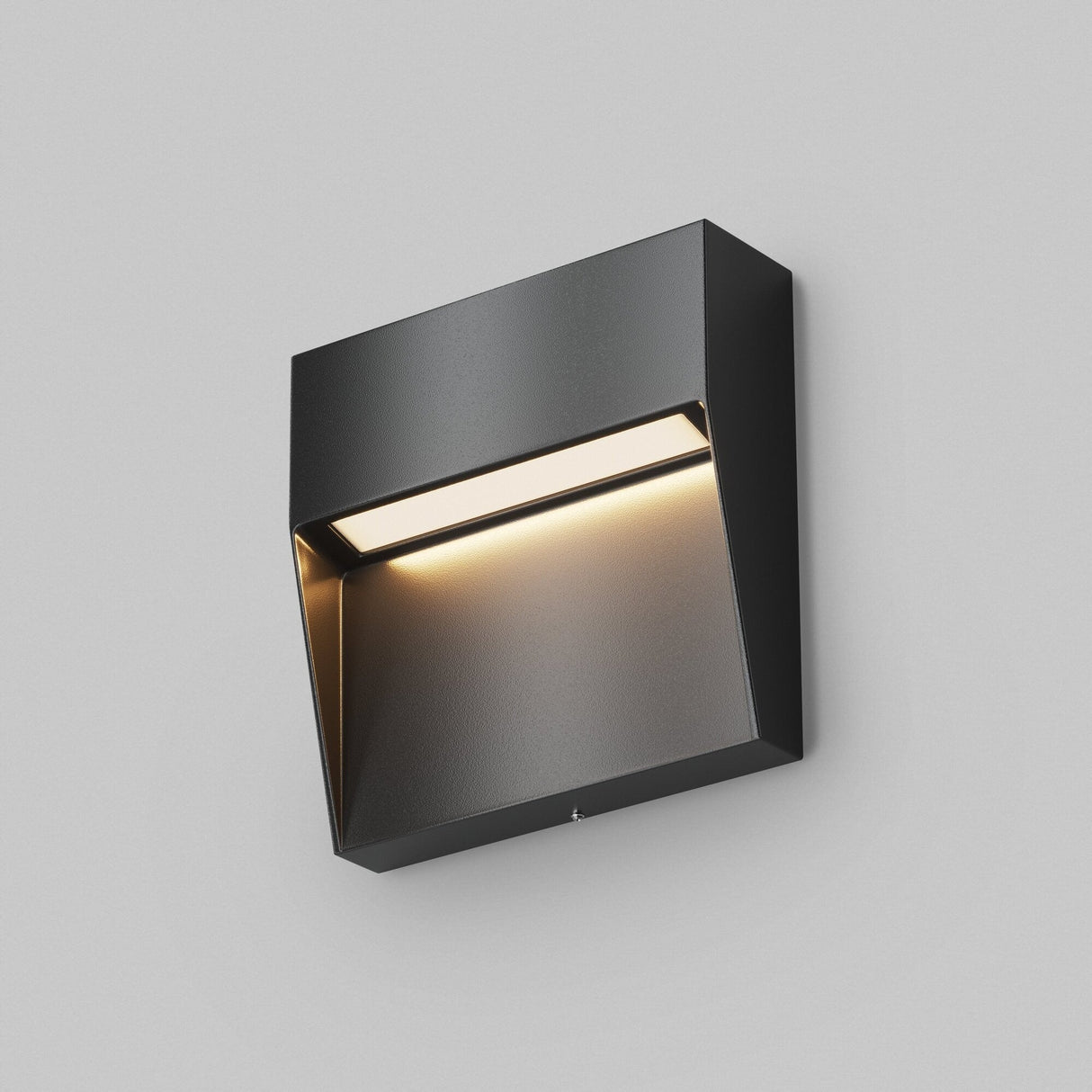 The Mane Outdoor LED Square Wall Light in black offers a sleek, minimalist design with energy-efficient lighting. It partially conceals a softly glowing bulb, casting warm light downward against a plain gray backdrop.