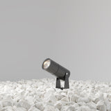 The Bern Outdoor LED Spike Light 5W 3000K - Graphite is crafted from corrosion-resistant aluminum, angled on white stones. Its sleek black design against a neutral gray background showcases energy-efficient LED technology.