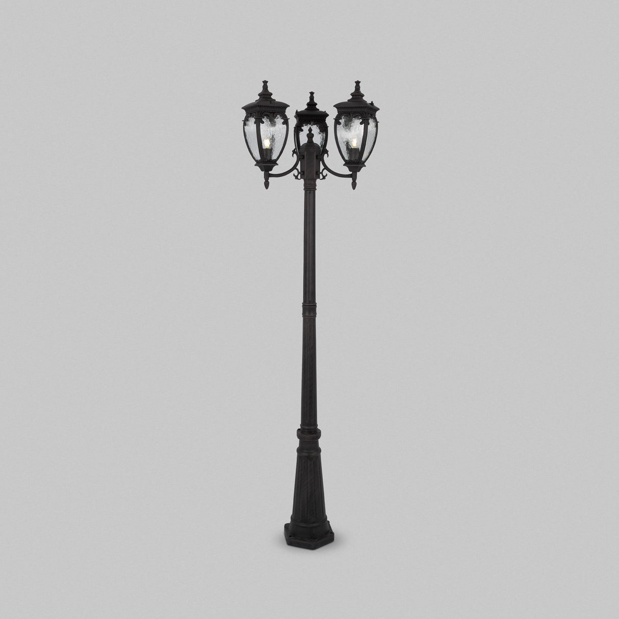 The Fleur 3 Light Triple Head Lamp Post - Bronze Antique is a vintage-style street lamp in black, featuring three ornate lanterns with clear glass panes. It stands on a square base with an antique bronze finish against a plain gray background.