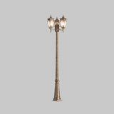 The Fleur 3 Light Triple Head Lamp Post features a tall, ornate design in gold and black. It is crafted from corrosion-resistant aluminum, adorned with three lanterns topped with decorative finials, and set against a plain gray background.