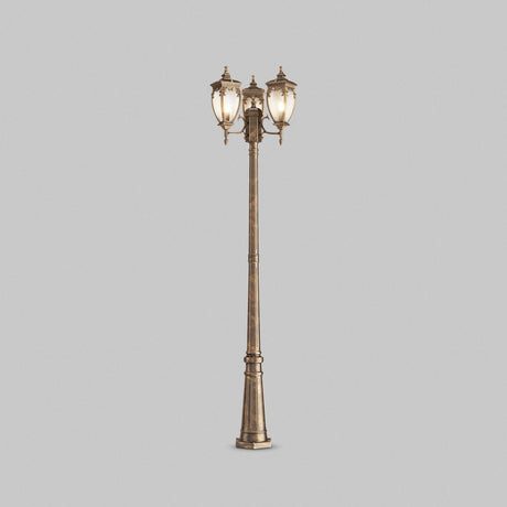 The Fleur 3 Light Triple Head Lamp Post features a tall, ornate design in gold and black. It is crafted from corrosion-resistant aluminum, adorned with three lanterns topped with decorative finials, and set against a plain gray background.