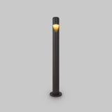 The Hagen LED Bollard Light 60cm in graphite is a minimalist outdoor lamp post with a warm glow near the top, set against a plain gray background. This sleek, cylindrical design embodies modern aesthetics and energy-efficient LED technology to enhance your outdoor space.