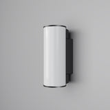 The Rock Outdoor LED Wall Light 3000K in Graphite is a sleek, modern LED wall light with energy efficiency and features a glossy white cylindrical body paired with black end caps, mounted on a light gray wall.