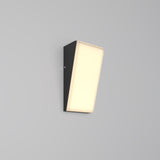 The Brick Outdoor LED Wall Light - Graphite (O436WL-L10GF3K1) features a sleek rectangular black fixture with a slanted illuminated front panel, emitting soft warm LED light. Its sophisticated graphite finish elegantly complements the plain light gray background.