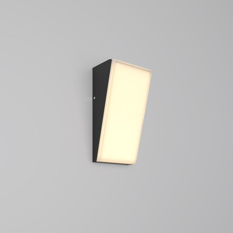 The Brick Outdoor LED Wall Light - Graphite (O436WL-L10GF3K1) features a sleek rectangular black fixture with a slanted illuminated front panel, emitting soft warm LED light. Its sophisticated graphite finish elegantly complements the plain light gray background.