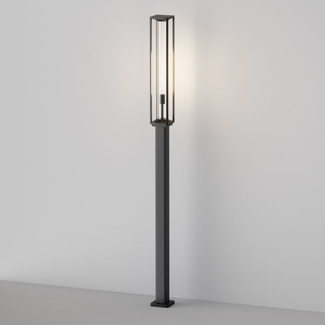 The Cell Bollard Light 220cm - Graphite features a tall, slim frame with a rectangular glass enclosure for soft ambient lighting. Placed against a stark white wall on a light surface, it perfectly captures modern minimalist design akin to sleek outdoor lighting.