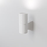 The Bowery Outdoor 1 Light Wall Light (O583WL-02W) in white features a textured cylindrical design and durable metal construction. Casting light upwards with a subtle matching bracket, it embodies an elegant, minimalist, contemporary aesthetic against a plain white wall.