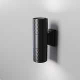 The Bowery Outdoor 2 Light Wall Light (O583WL-02B) is a black, modern metal fixture with a textured diamond pattern, mounted on a gray wall. Its cylindrical design emits light from both ends, making it an ideal sleek and minimalistic choice for any outdoor setting.