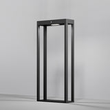 A modern, sleek graphite standing lamp with an open rectangular design sits against a plain gray background. The Pir LED Pedestal Light with Motion Sensor at the top softly illuminates the interior with a stylish glow.
