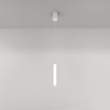 A minimalist white ceiling features the Ray LED Short Pendant Light in white, casting a soft glow. This modern interior creates a sleek ambiance against the plain background, epitomizing minimalist lighting design with its slender cylindrical form.