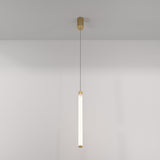 The Ray LED Long Pendant Light - Gold & White hangs by a thin cord, featuring a cylindrical beige mount and frosted tubular light fixture with matte gold accents. It complements the plain, light-colored wall with its minimalist design.