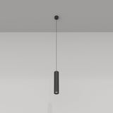 The Focus Single Pendant Light - Black hangs gracefully from the ceiling with its black metal finish, casting light downward. It highlights a modern industrial aesthetic against the smooth white wall, emphasizing simplicity and elegance in design.