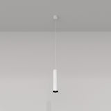 The Focus Single Pendant Light - White features a sleek, minimalist design that gracefully hangs from the ceiling, casting subtle shadows on the wall. Ideal for modern interiors, its cylindrical shape adds elegant charm to a plain gray backdrop.
