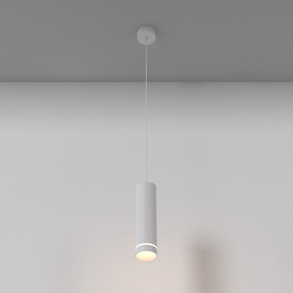 The Orlo LED Pendant Light 3000K in white, with its minimalist cylindrical design and adjustable suspension, casts a soft glow from the ceiling. It complements the simple light gray wall, ideal for contemporary interiors.