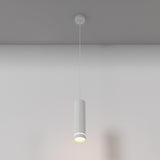 The Orlo LED Pendant Light 3000K in white, with its minimalist cylindrical design and adjustable suspension, casts a soft glow from the ceiling. It complements the simple light gray wall, ideal for contemporary interiors.