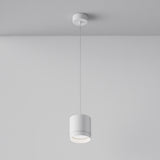 The Polar Short Round Pendant Light - White elegantly hangs from the ceiling, casting a warm glow that enhances modern interiors and gently illuminates the smooth, plain wall around it.