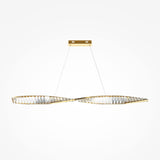The Krone LED Long Crystal Linear Suspension Light - Brass showcases a modern design with two intertwined, elongated brass loops and translucent materials. It hangs from thin wires connected to a rectangular gold ceiling mount, set against a plain white background.