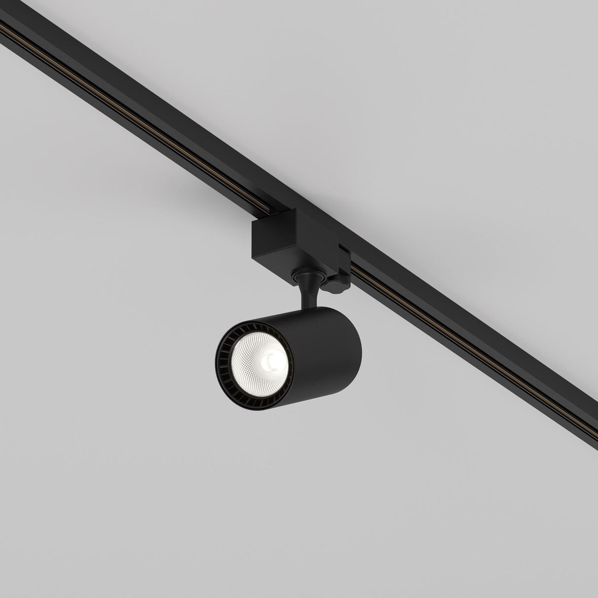 The Vuoro S 3-Circuit Trinity Track LED Spotlight, 10W 4000K in black, features a cylindrical design with an adjustable swivel head and is mounted on a 3-circuit track rail, casting downward light against a white ceiling.